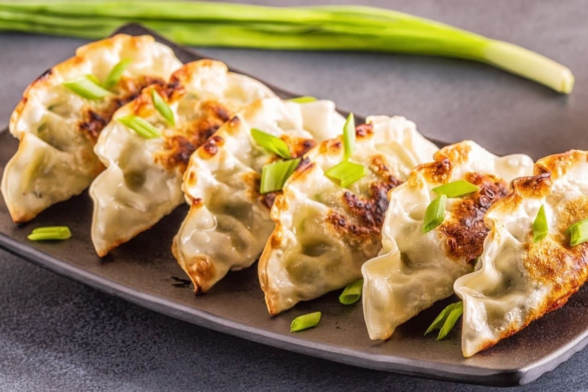 Hjemmelagde gyoza dumplings med gyllen sprø bunn, servert på tallerken med dippsaus og friske urter
